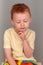 Fiery redhead young boy in yellow shirt looking down, fist to chin in deep thought, portrait format on grey background with copy