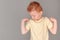 Fiery redhead young boy in yellow shirt looking at right arm with strong arms pose. Landscape on grey with copy space left.