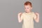 Fiery redhead young boy in yellow shirt trying to pose with strong arms