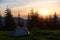 Fiery sunset in mountains. One tent is surrounded by small firs against the backdrop of mountains