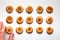 Fifteen handmade cookies with apricot jam arranged in even rows on white background. Man hand takes one from down