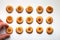 Fifteen handmade cookies with apricot jam arranged in even rows on white background. Man hand takes one from side