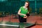 Fifteen-year-old beautiful Caucasian teen girl in a green sports t-shirt holding a tennis racket and a ball and looking at the