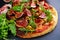 Fig pizza with bacon, green pimiento olives, rocket and basil leaves