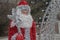 Figure of Santa Claus in form of mannequin with white beard in a shiny fluffy red fur coat with fringe with white staff with star