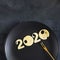 Figures 2020 made of cheese with holes on a black plate with small gold fork on chalk board background, top view, Square