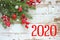 Figures 2020 on a white wooden background, frame of fir branches and red berries, Christmas background, postcard,