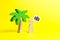 Figurine of a man with a poster with a bag under a palm tree on a yellow background. Concept of wanting a vacation trip