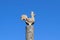 Figurine of a rooster on a tree stump on a background of blue sky. Figures of animals made of wood. Woodcarving