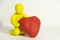 Figurine yellow plasticine man holding a red heart in hands