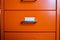 Filing cabinet with closed drawer, A white card for write letter, Orange metal colour, Administration and storage concept, closeup