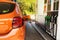 Fill car with fuel in petrol station. Pumping gasoline fuel in orange car at a gas station in city