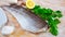 Fillet of raw codfish on a wooden surface with garlic and greens