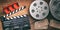 Film reels with retro cinema tickets, movie clapper and red theater seats on wooden background. 3d illustration.