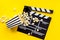 Filmmaker profession with clapperboard and popcorn on yellow background top view