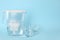 Filter jug and glasses with purified water on light blue background. Space for text