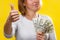 Finance, loans and banking. Close up of a young blonde holds a wad of dollars in her hands and gives a thumbs-up, smiling. Yellow