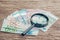 Finance saving, tax, investment or searching for yield concept, magnifier glass on pile of Euro banknotes on wooden table,