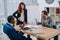 Financial adviser standing near table with laptop and papers while two businessmen arguing