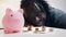 Financial decision, investments and savings. African american man looking into the coins in front of the piggy bank.