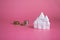 Financial growth concept, money saving planning. Close-up of a castle house and stacks of coins on a pink background. Saving or