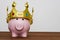 Financial winner or king of money savings concept, smiling happy pink piggy bank wearing a golden crown on wooden table, best futu