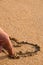 Finger draws a love heart in the sand