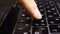 The finger presses the dusty button of the laptop keyboard