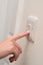 Finger Presses Light Switch on Wall Next to Door