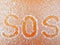 Fingerprint `SOS` on hoarfrost on an orange surface. A person`s request for help.