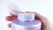 Fingers close lid of purple bottle. Jar of shampoo, hair conditioner, shower gel, bath foam, moisturizing skin lotion. Natural