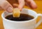 Fingers hold a lump sugar piece over cup of tea