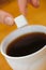 Fingers hold a lump sugar piece over cup of tea