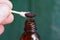 Fingers hold a wand with a cotton swab in brown iodine over an open opened bottle