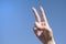Fingers shape the Victory sign against of woman hand with blue sky