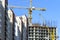 Finished Apartment Building and a New High-Rise Building Construction Site with Yellow Cranes against Blue Sky. Real Estate,