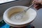 The finished pancake batter in a white bowl with a metal whisk holds the woman`s hand of an elderly woman