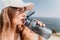 Fintess woman drinking water. Happy, active middle aged woman standing on beach and drinking water after excersise