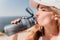 Fintess woman drinking water. Happy, active middle aged woman standing on beach and drinking water after excersise