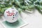 Fir tree toy ball decorated with joyful snowman on Christmas card next to fir tree branches on white textured background
