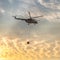 A fire fighter helicopter with a full basket of water flies against a beautiful sunset sky