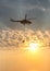 A fire fighter helicopter with a full basket of water flies against a beautiful sunset sky