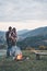 Fire keeps them warm. Handsome young man embracing his attractive girlfriend while standing near the campfire outdoors