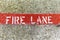 Fire Lane painted on a Curb in White Lettering and Red Background on Textured Concrete Pavement