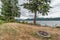 Fire pit and picnic table in grass lawn on lake edge and boat trees evergreen Bellingham