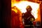 Fire on wall and ceiling in the kitchen behind firefighter man with protective and safety clothes stand with arm-crossed