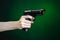 Firearms and murderer topic: human hand holding a gun on a dark green background isolated in studio