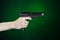 Firearms and murderer topic: human hand holding a gun on a dark green background in studio