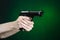 Firearms and murderer topic: human hand holding a gun on a dark green background in studio