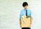 Fired dismissed young Asian employee with cardboard brown box filled with his personal belongings